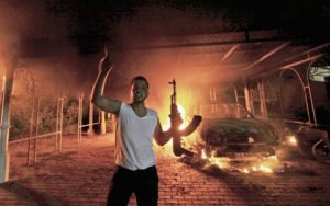 A protester reacts as the U.S. Consulate in Benghazi is seen in flames during a protest by an armed group said to have been protesting a film being produced in the United States September 11, 2012. An American staff member of the U.S. consulate in the eastern Libyan city of Benghazi has died following fierce clashes at the compound, Libyan security sources said on Wednesday. Armed gunmen attacked the compound on Tuesday evening, clashing with Libyan security forces before the latter withdrew as they came under heavy fire. REUTERS/Esam Al-Fetori (LIBYA - Tags: POLITICS CIVIL UNREST TPX IMAGES OF THE DAY)
